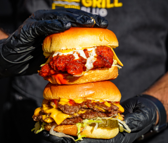 Smash burgers, wings and shakes for delivery at The Grill Plug Cambridge Person holding two burgers on top of each other, man is wearing a Grill Plug T shirt