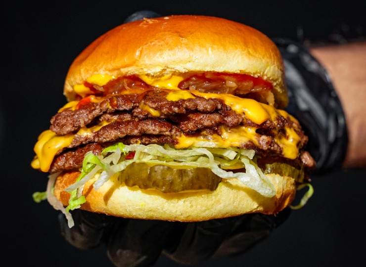 Smash beef burger with melting cheese and lettuce, held by man with black gloves